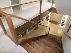 curved walnut staircase, cream carpet, glass balustrade
